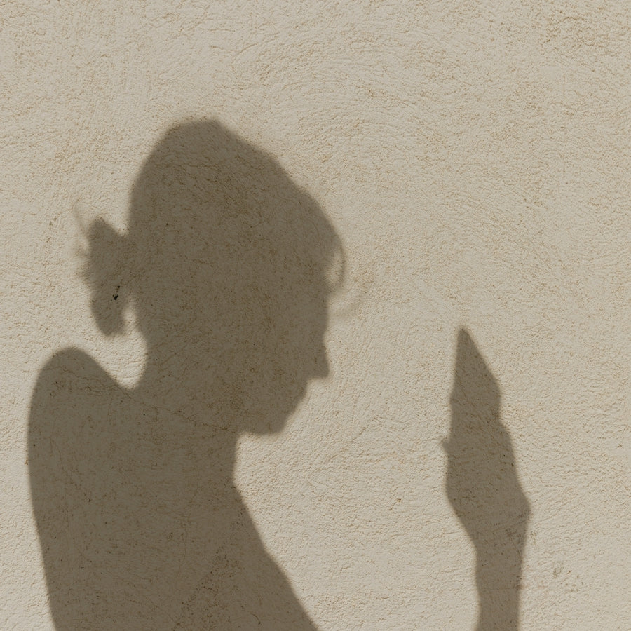 Silhouette of a person holding a phone and looking at it against a textured plaster wall