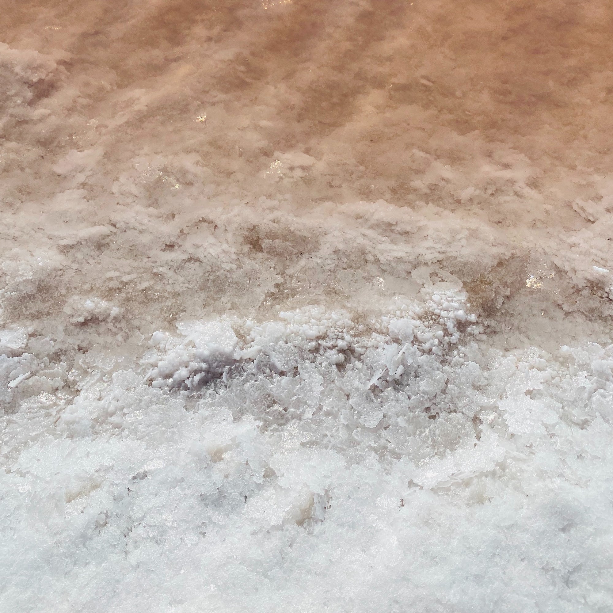 Close-up of unrefined salt crystals showing coarse flaky texture and pale pink-brown mineral layers
