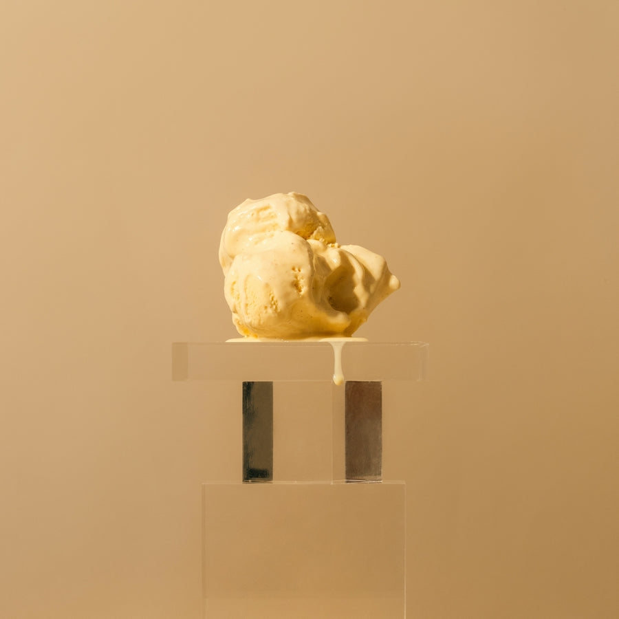 Scoop of melting vanilla ice cream on a clear pedestal against a beige background