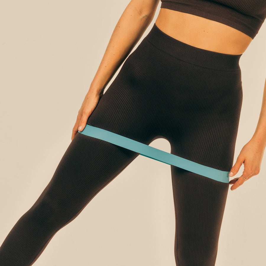 Person wearing black ribbed leggings using a blue resistance band around their thighs for exercise.