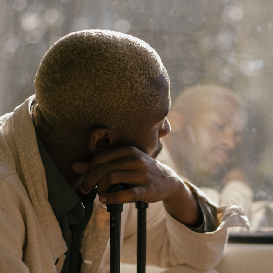 Person leaning on crutches while looking out a window, with their reflection visible