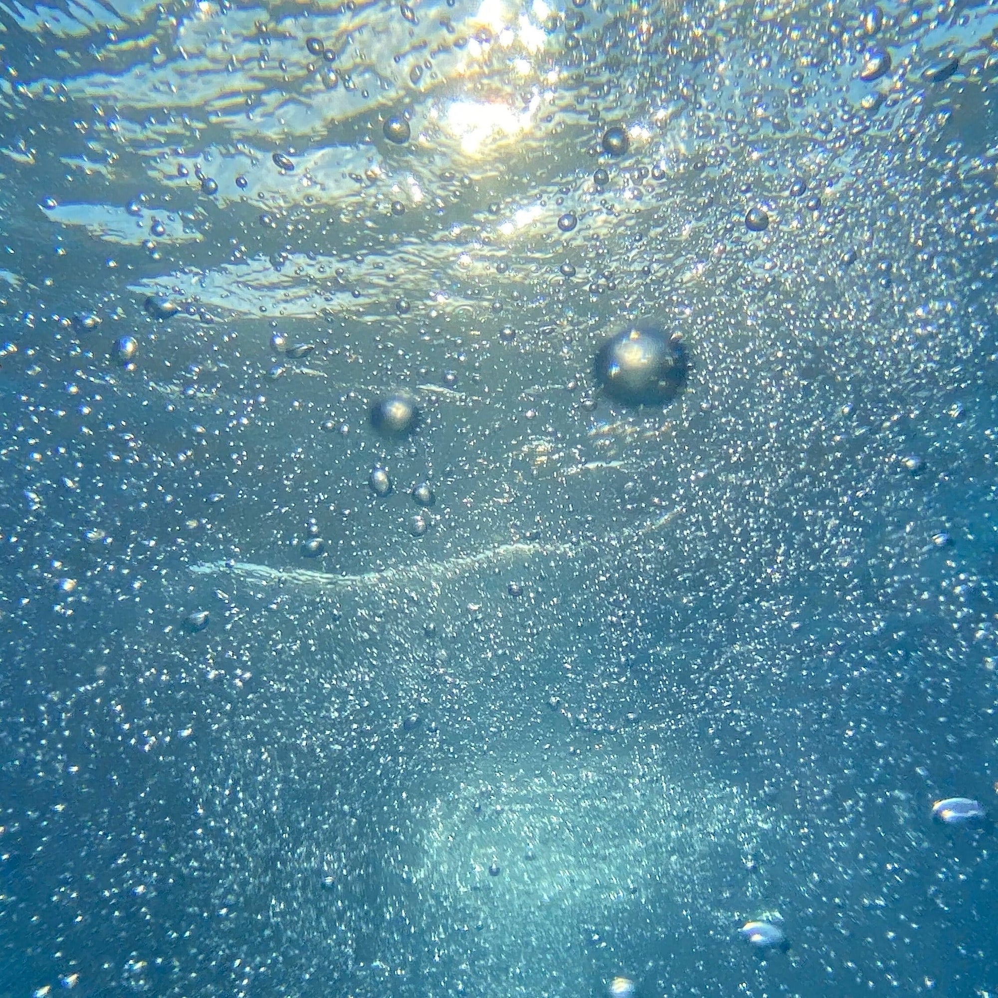 Sunlit underwater view with many rising air bubbles in clear blue water