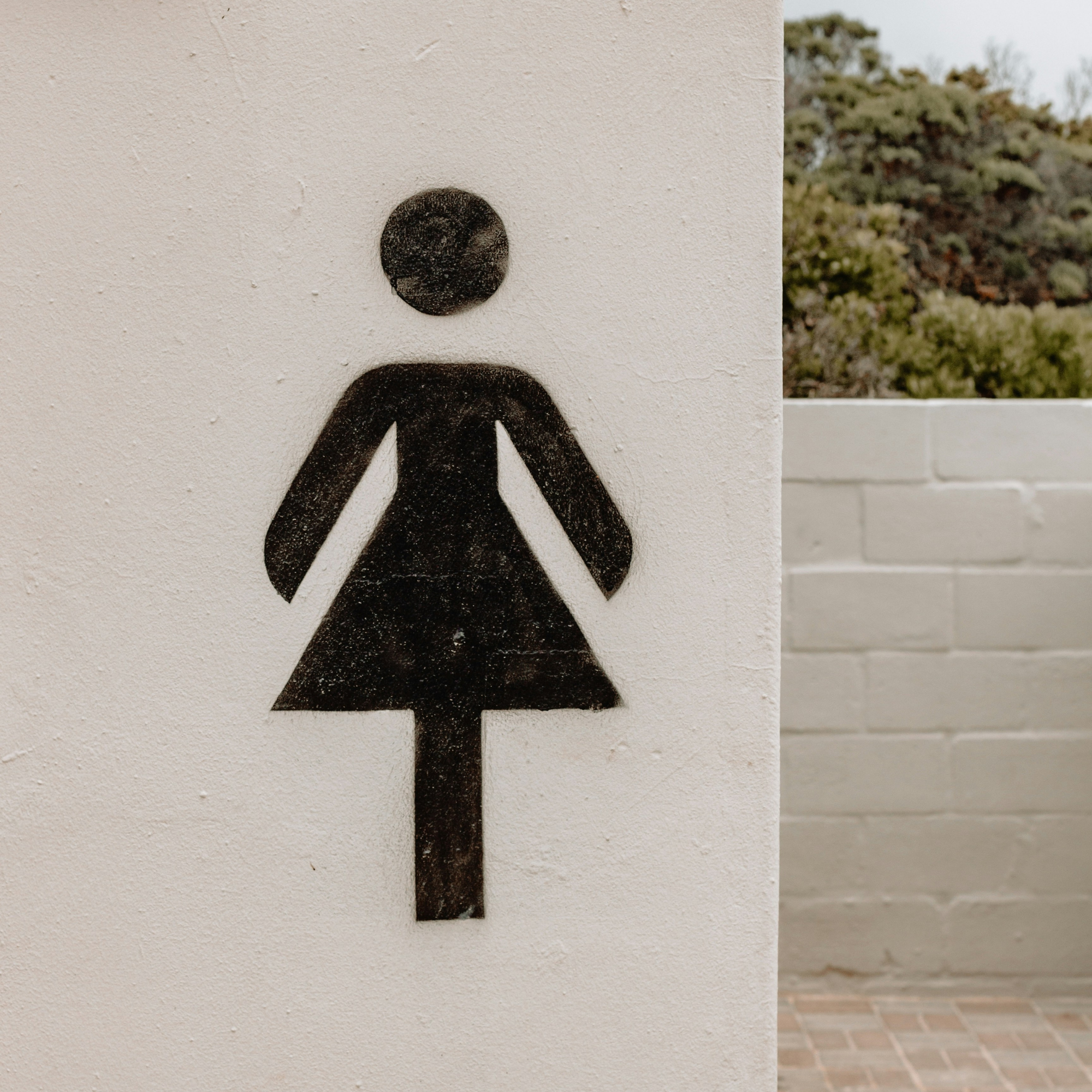 Women’s restroom symbol mounted on a wall beside an outdoor walkway