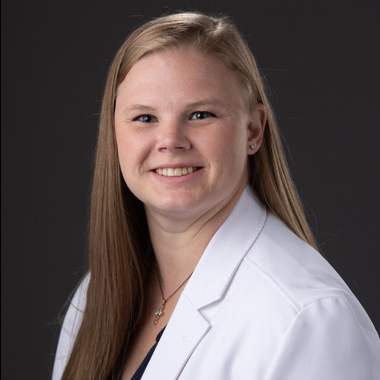 Portrait of Dr. Alex Shurling in a white medical coat against a dark background