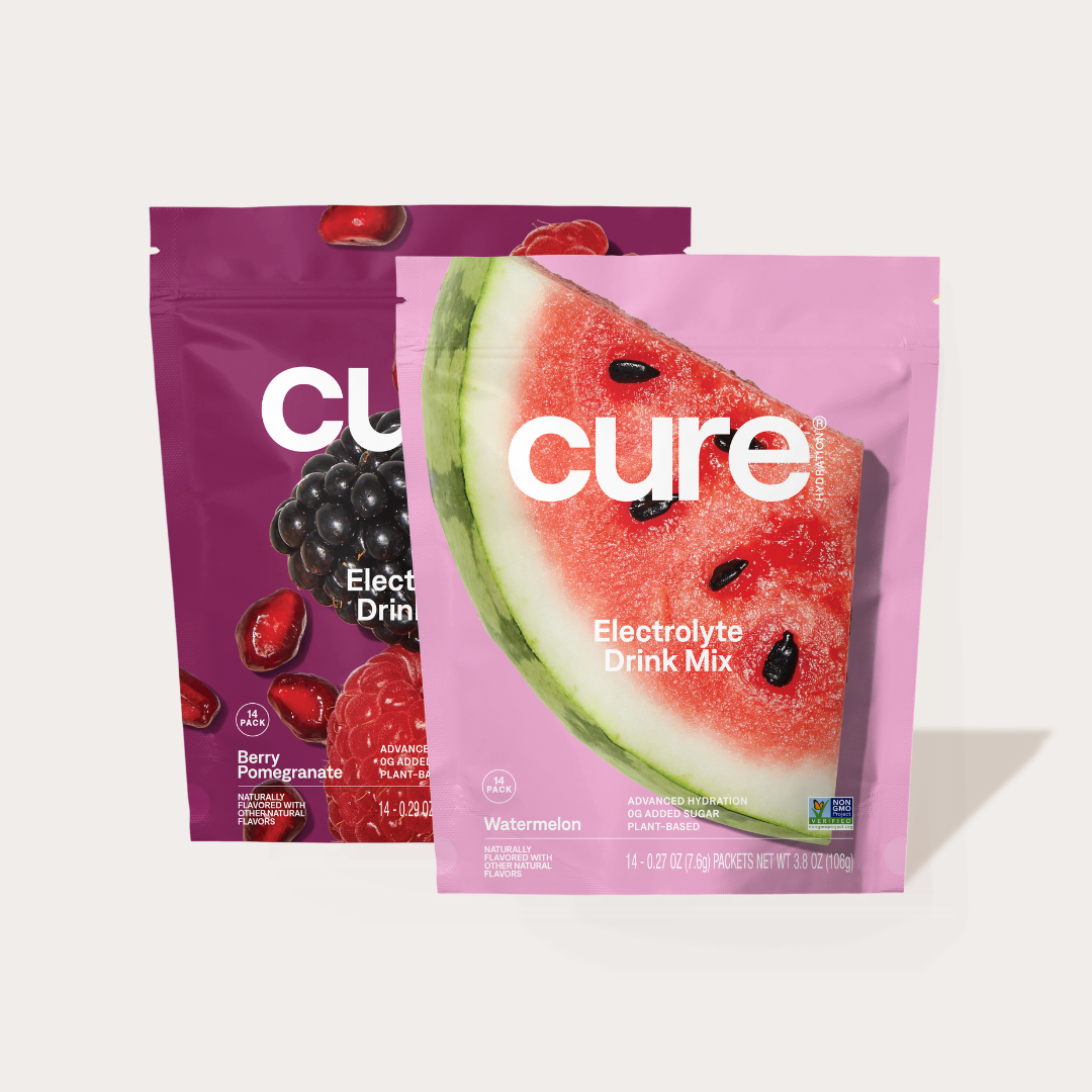 Two Cure Electrolyte Drink Mix packets, one Watermelon flavor with a watermelon slice image and one Berry Pomegranate flavor with berries and pomegranate seeds on the packaging.
