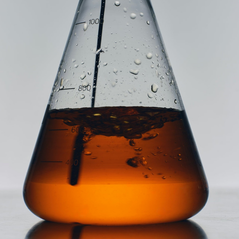 Conical flask with orange Cure Hydration liquid and water droplets on a gray background