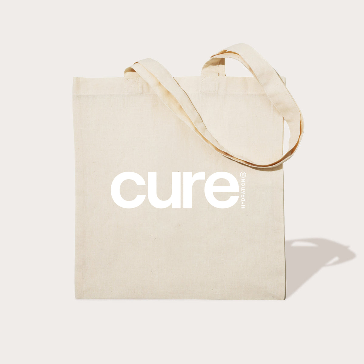 Beige tote bag with the word 'cure' printed in large white letters on the front.