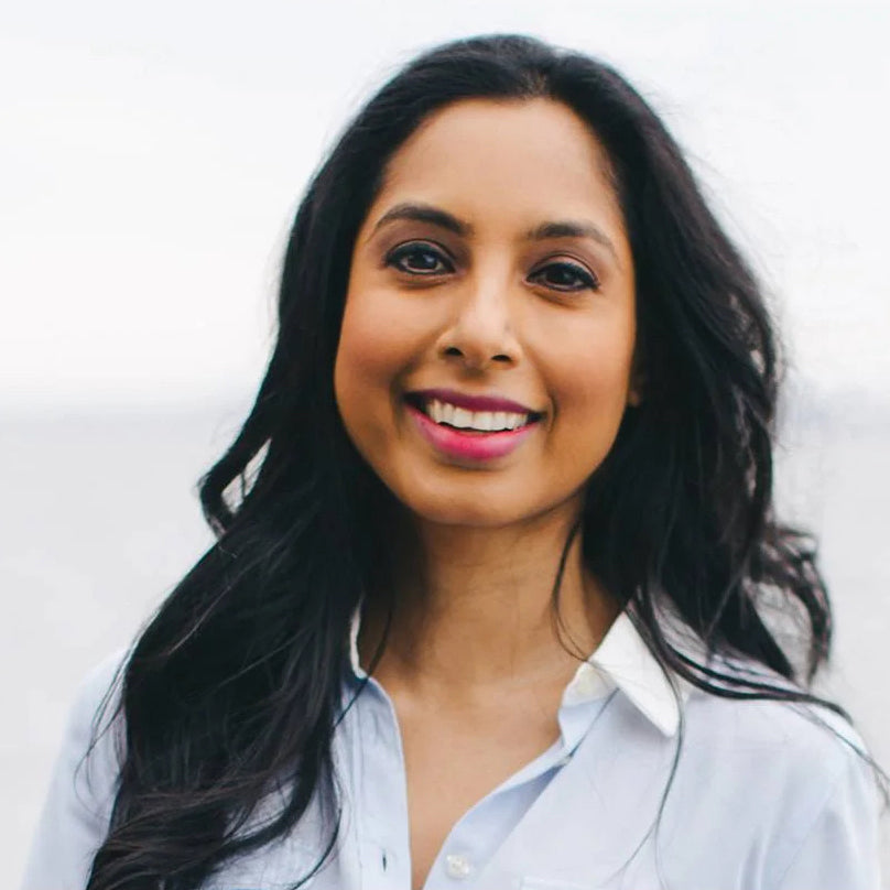 Portrait of a smiling woman with long black hair in a blue shirt, with a soft, misty background.