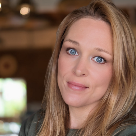 Close-up portrait of a woman with light brown hair, blue eyes, wearing a green top.