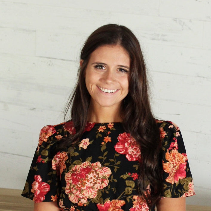 Cheerful woman with long brown hair in a black floral dress.