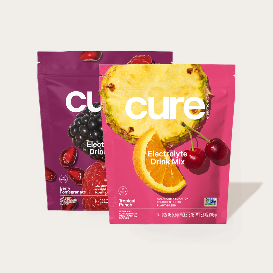 Two Cure electrolyte drink mix packets: Tropical Punch with pineapple, orange, and cherry images, and Berry Pomegranate with pomegranate and blackberry images.