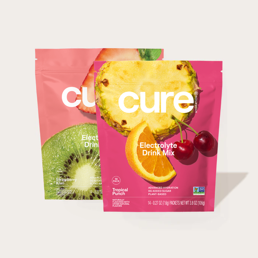 Two Cure electrolyte drink mix packets, Tropical Punch and Strawberry Kiwi flavors, with images of pineapple, orange, cherry, and kiwi fruits on the packaging.