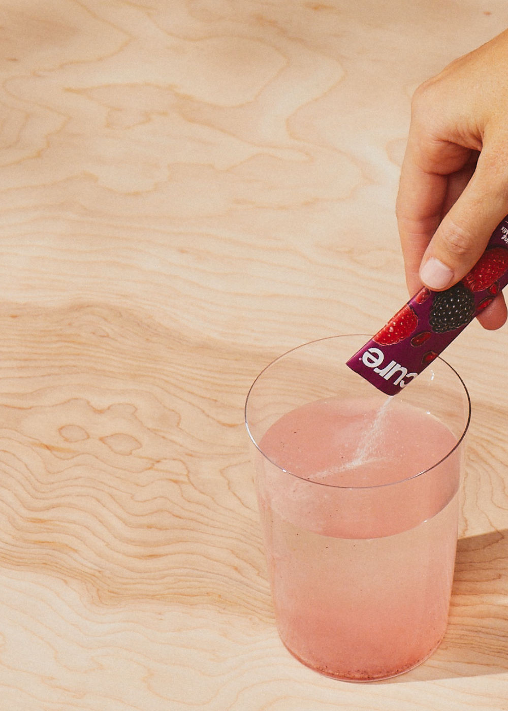 Hand pouring red 'Cure' powder into water, making a pink swirl on wood.