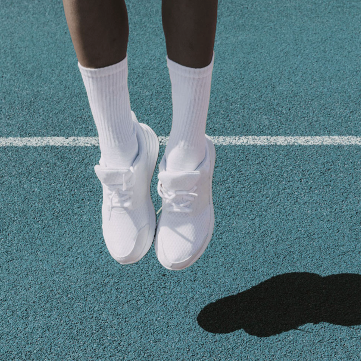Runner's lower legs jumping on a blue track wearing white running shoes and crew socks