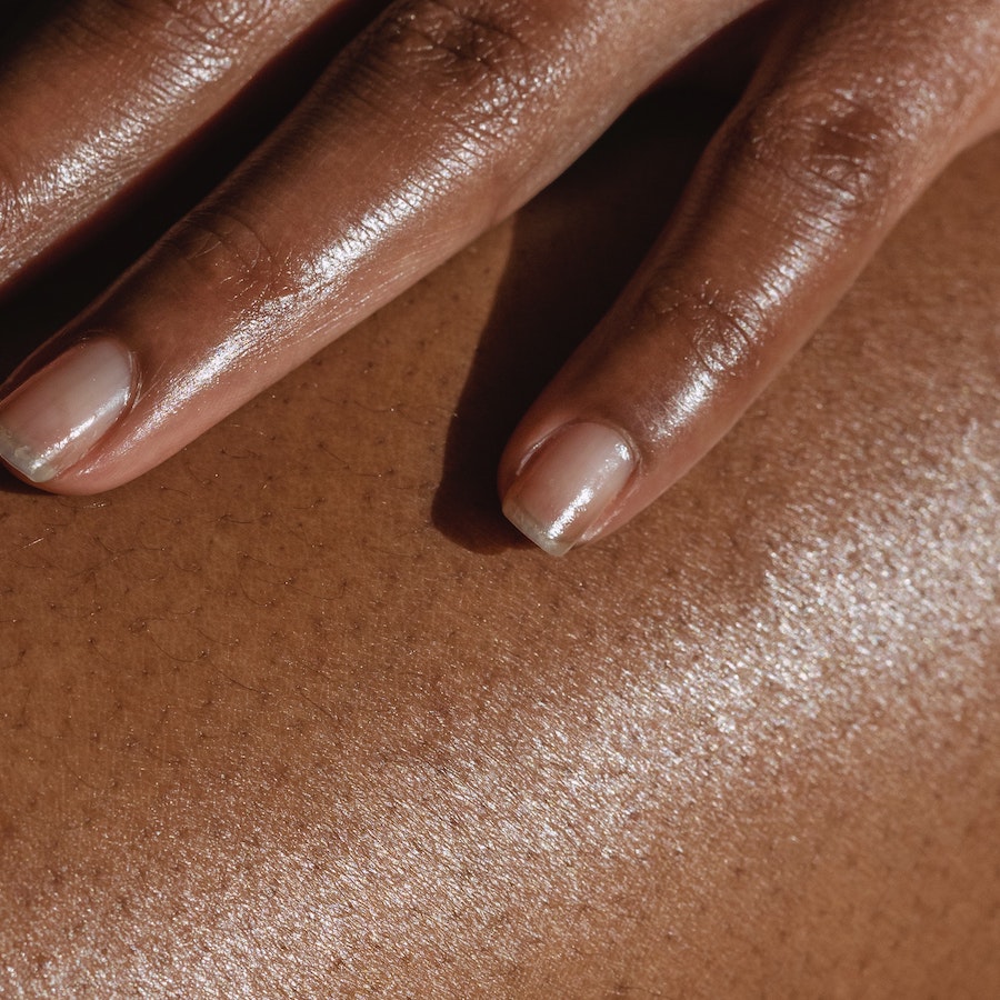 Close-up of hydrated dark skin with two fingers resting gently, showing smooth texture and shine.