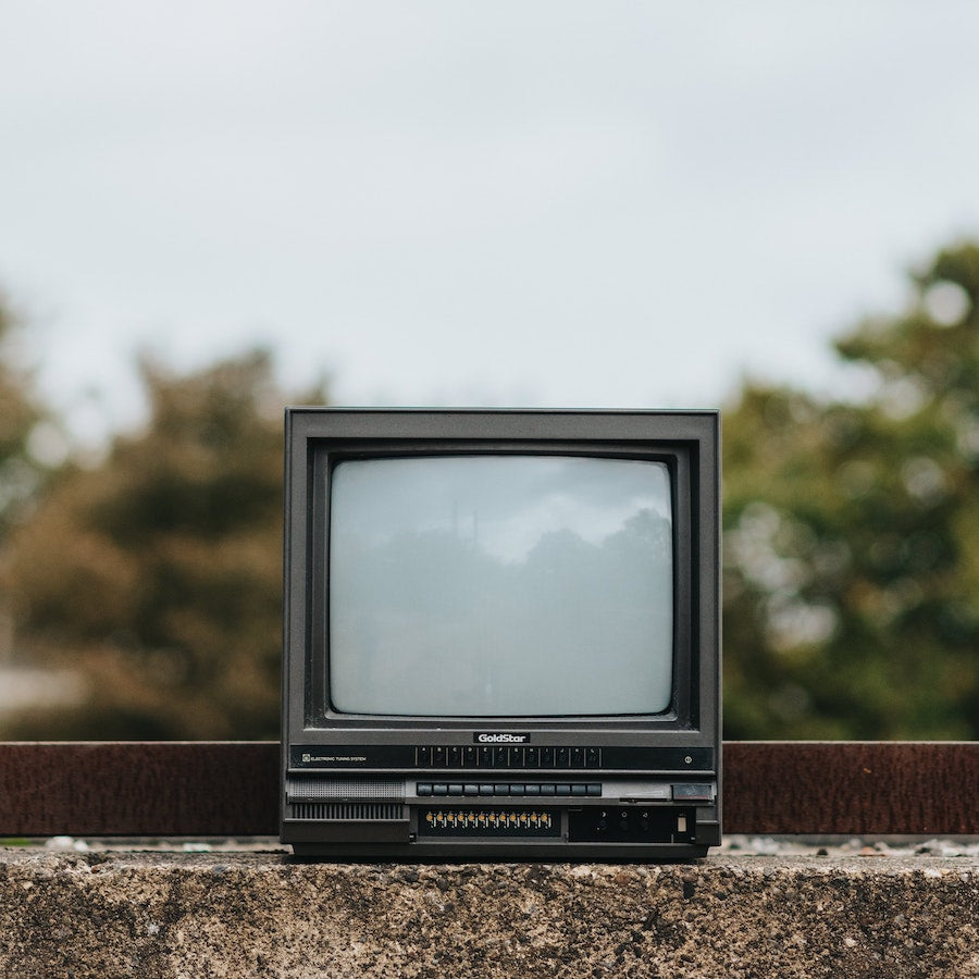 Old GoldStar CRT television with blank screen sitting on a stone surface outdoors, with blurred trees in the background. 