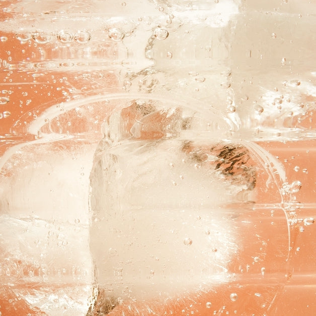 Close-up of ice cubes submerged in a fizzy liquid with bubbles rising, against a warm peach background.