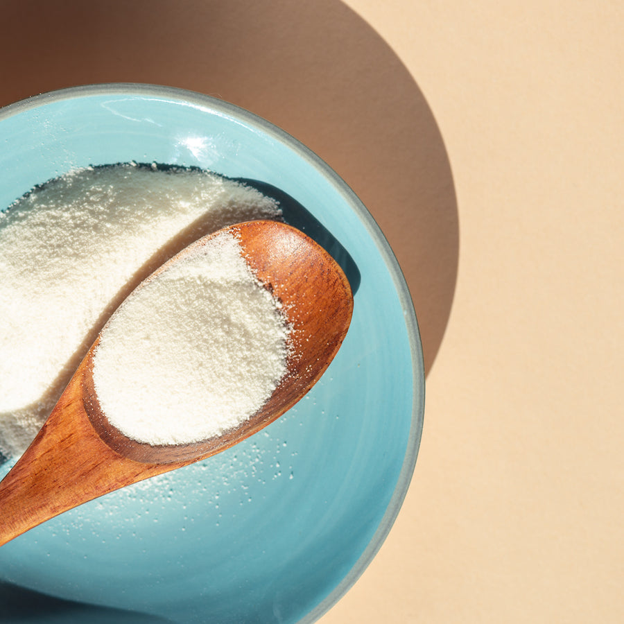 Wooden spoon filled with white electrolyte powder resting on a blue bowl against a beige background