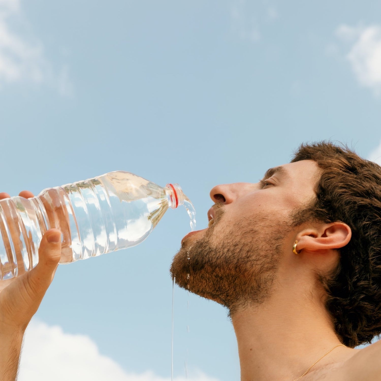 Man drinking water from a clear plastic bottle outdoors against a blue sky.