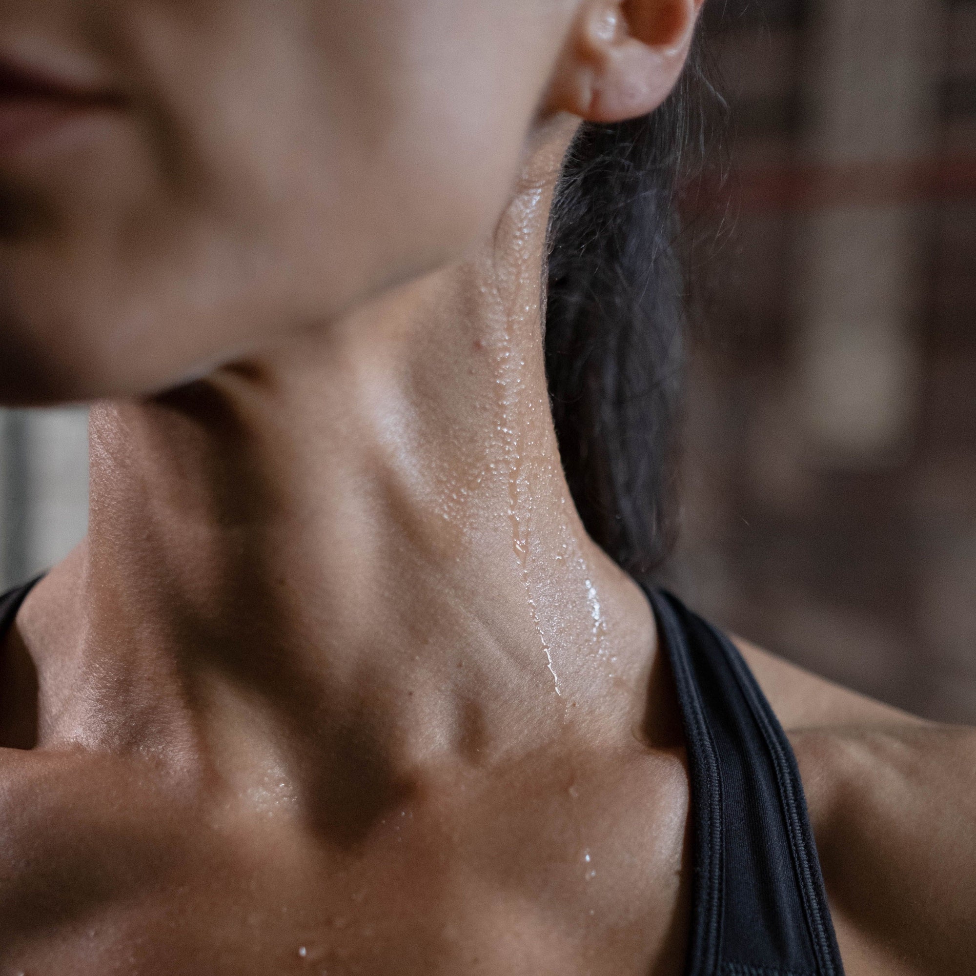 Close-up of a woman’s neck and shoulder with sweat running down her skin after a workout in a gym