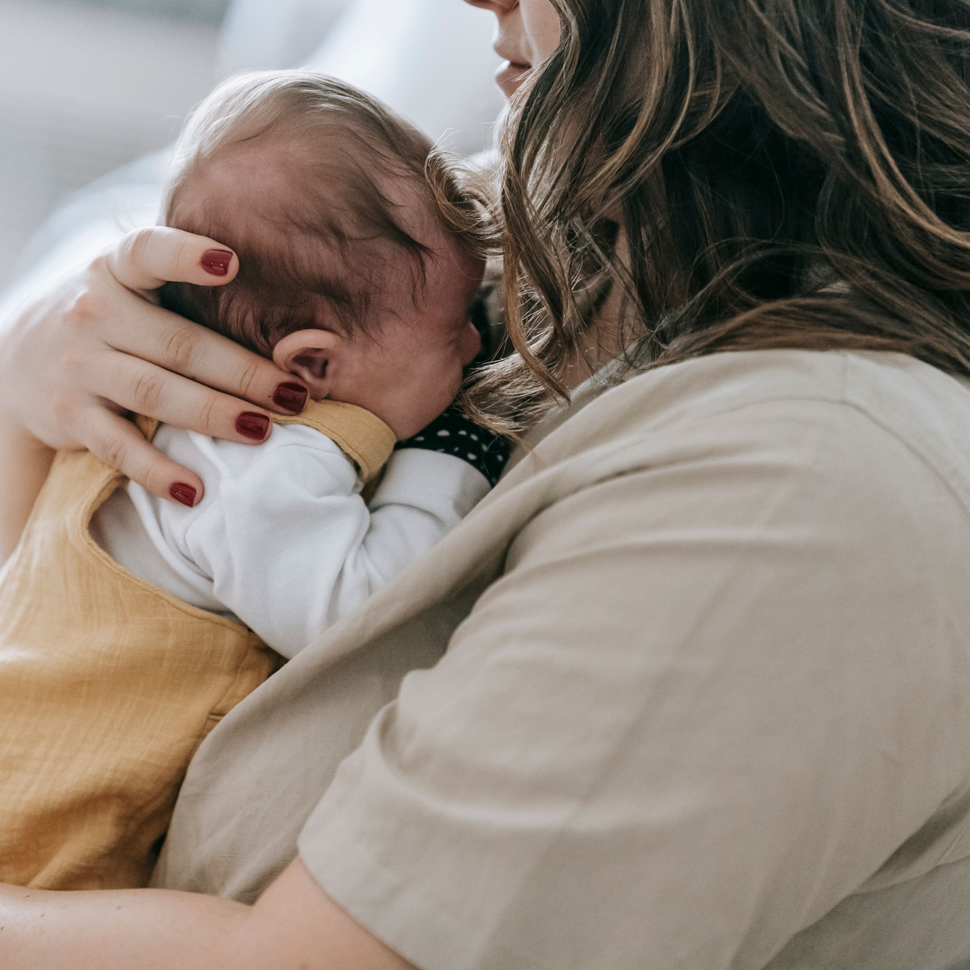 Mother holding newborn against her chest in a softly lit home interior