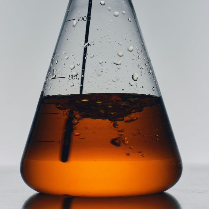 Conical flask with orange Cure Hydration liquid and water droplets on a gray background