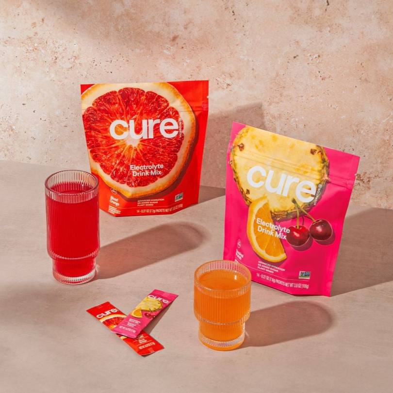 Cure electrolyte drink mix packets and glasses on a beige surface