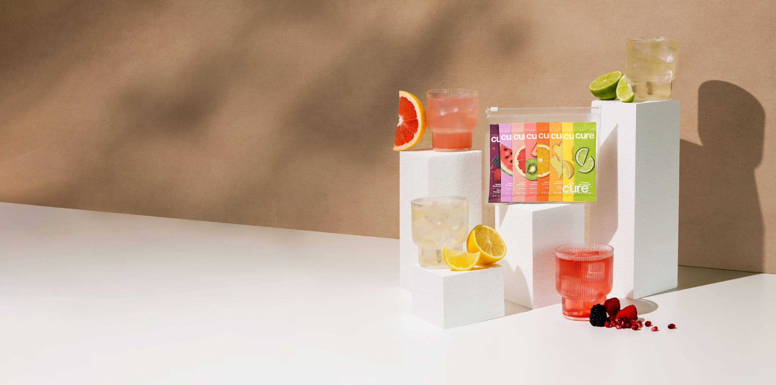 'Cure' drinks on pedestals: grapefruit, pink, lemon, lime flavors, beige background.