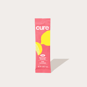 Single-serve pink 'cure' packet with lemon graphics labeled 'Electrolyte Drink Mix' flavor 'Pink Lemonade'.
