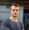 Confident young man with short brown hair in a dark blue t-shirt, smiling slightly.