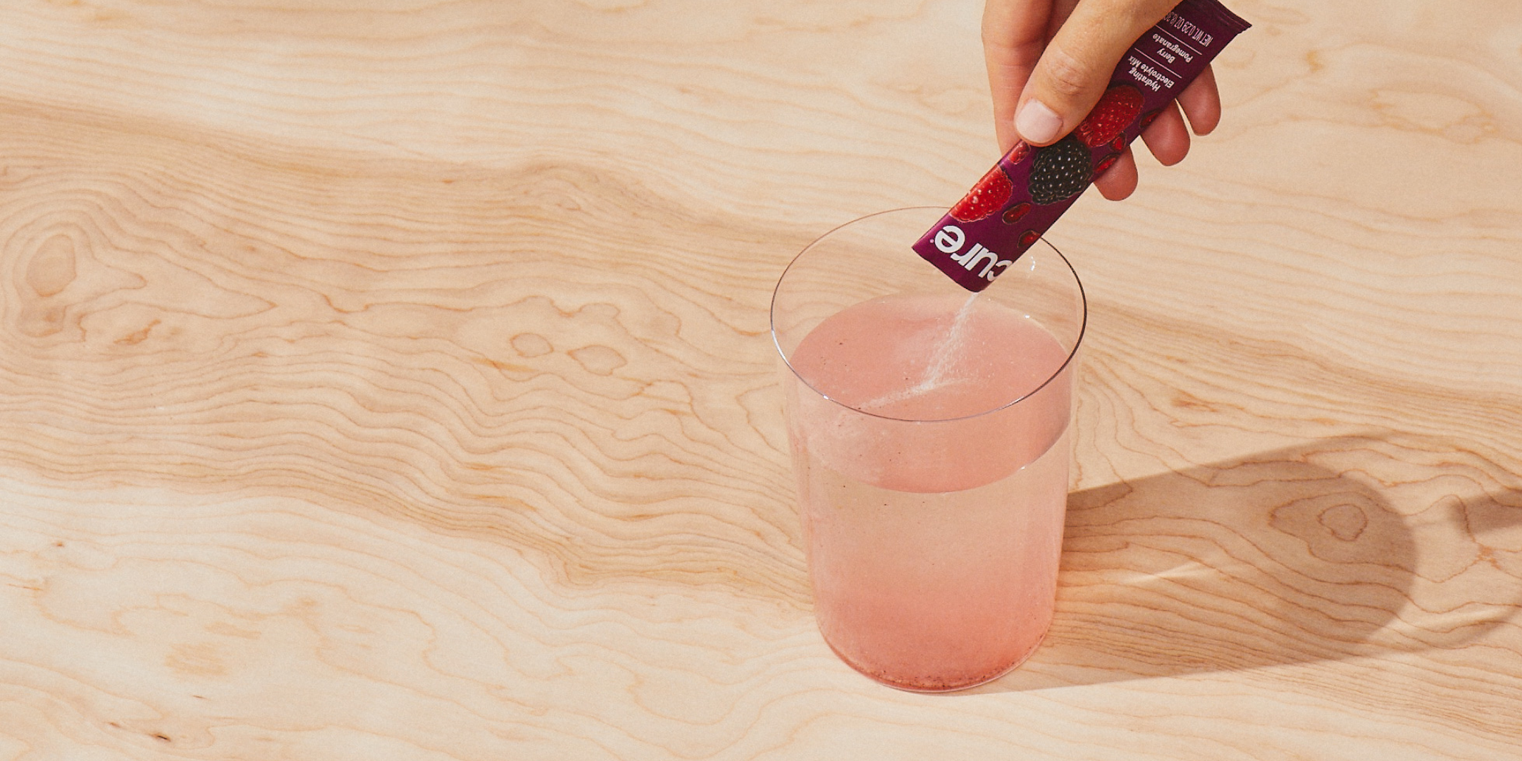 Hand pouring red 'Cure' powder into water, making a pink swirl on wood.