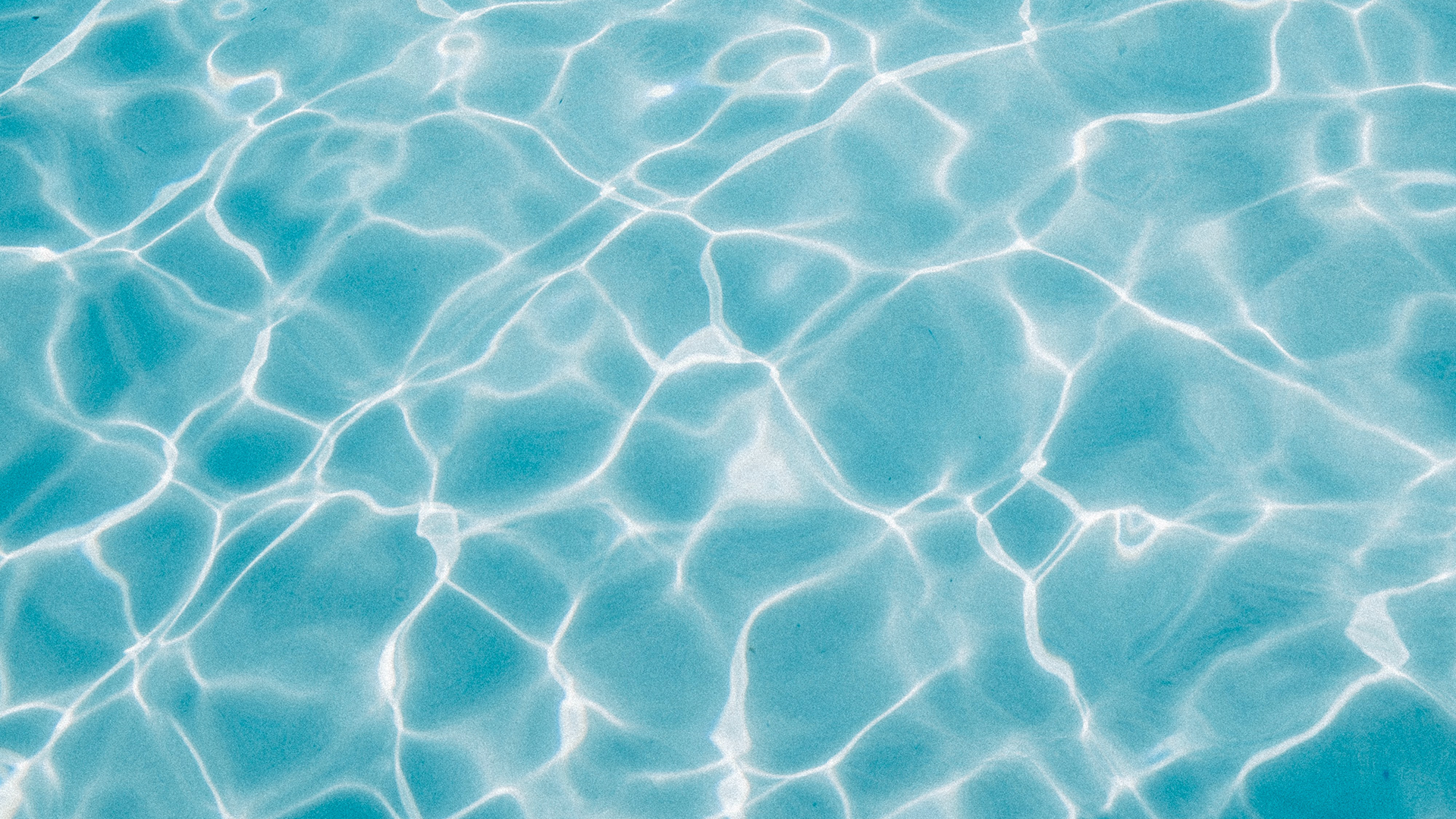 Sunlit turquoise pool water surface with rippling light reflections.