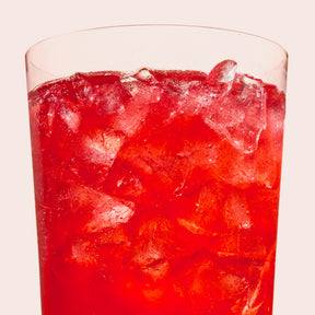 Close-up of Blood Orange electrolyte drink showing bright red liquid and crushed ice in a clear tall glass on pale pink background