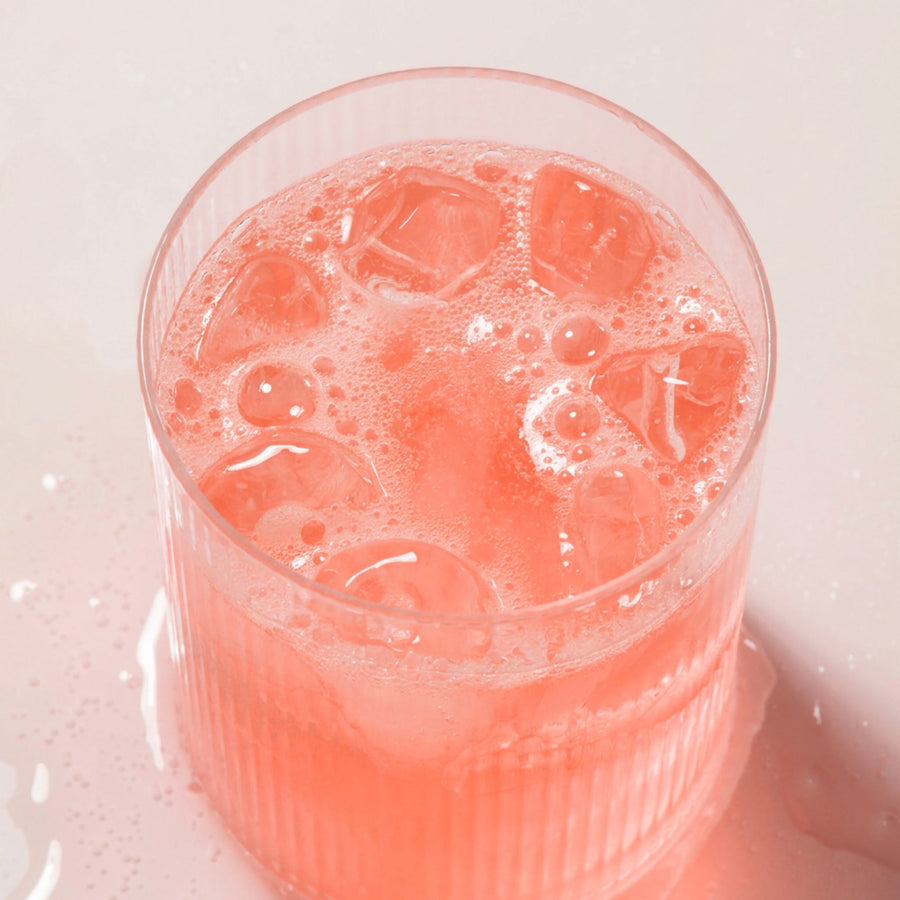 Top-down view of Mixed Berry electrolyte drink in a ribbed glass showcasing pink color, ice, and bubbles on a pale pink surface