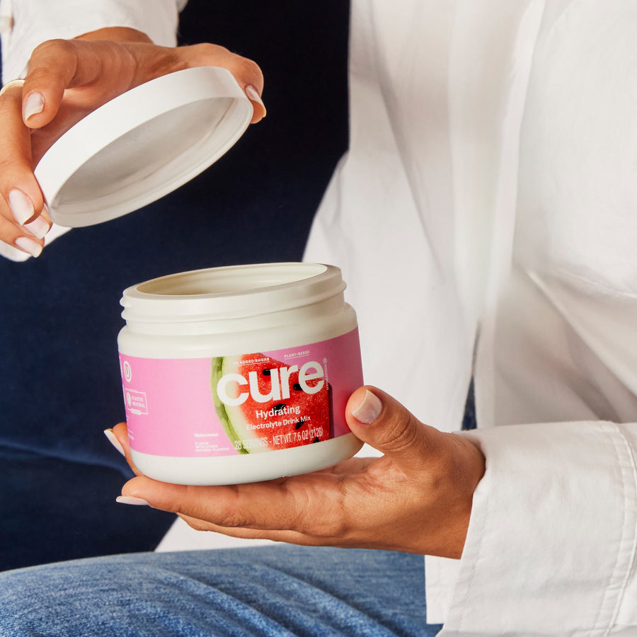 Close-up of Watermelon Bulk Jar showcasing open lid and pink Cure label held in hands against a white shirt background