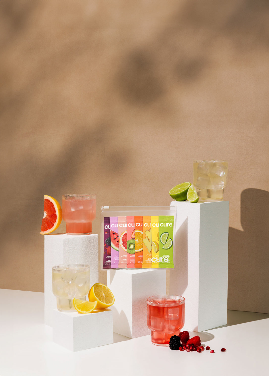 'Cure' drinks on pedestals: grapefruit, pink, lemon, lime flavors, beige background.
