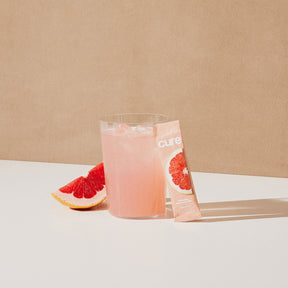 Pink grapefruit drink with mix packet and citrus fruit.